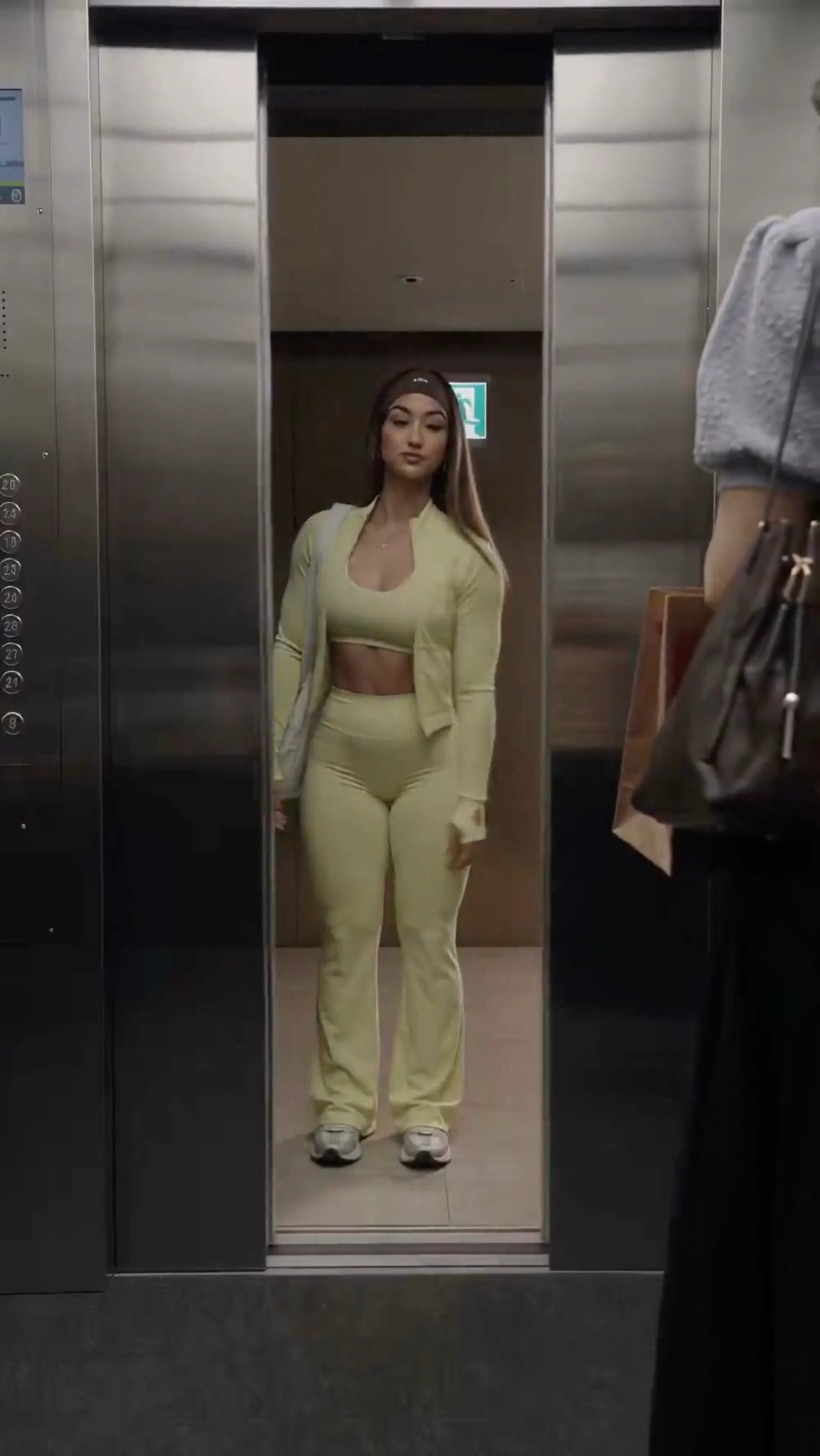 AI-generated model in sage activewear standing in an elevator, still from the video ad