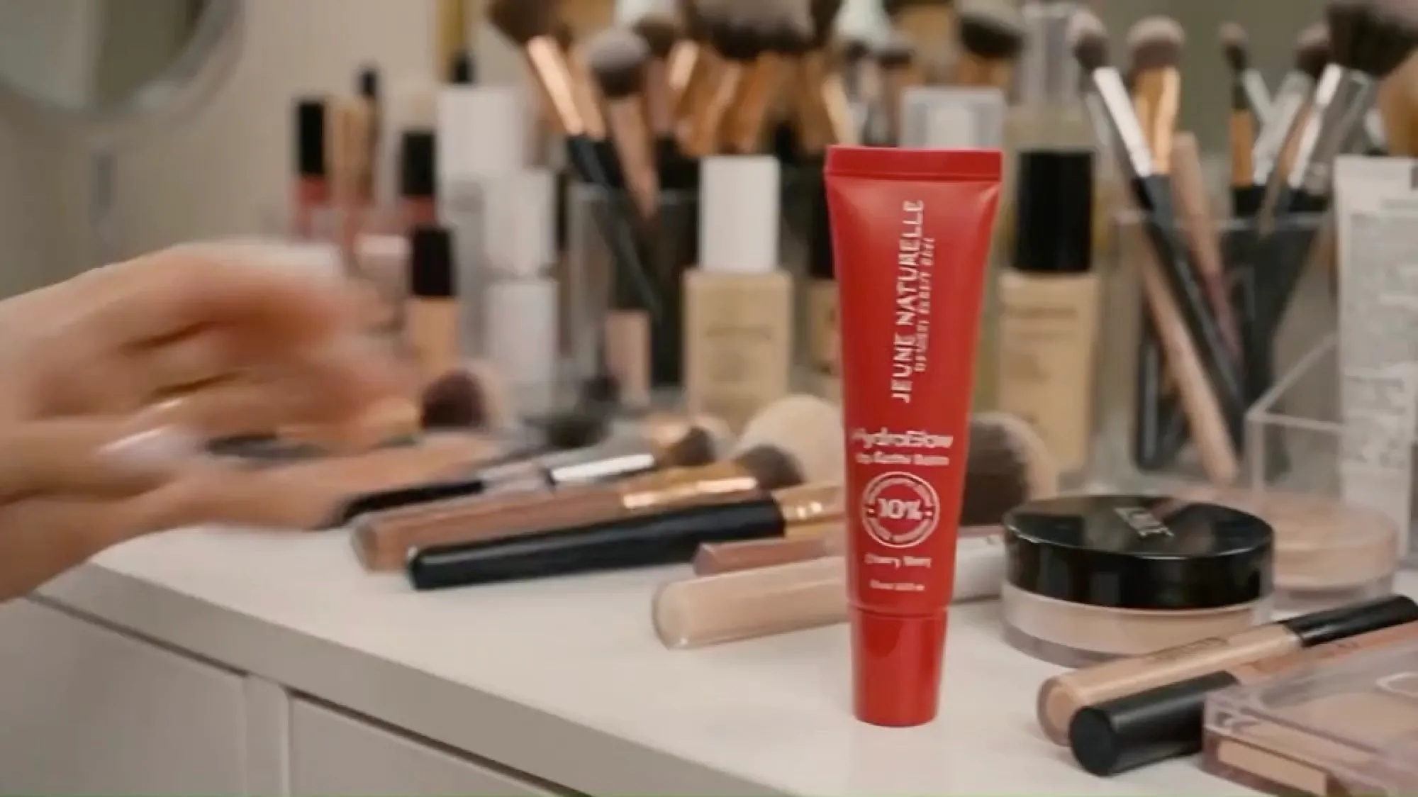 Lip balm on a vanity among makeup products, opening shot of the ad